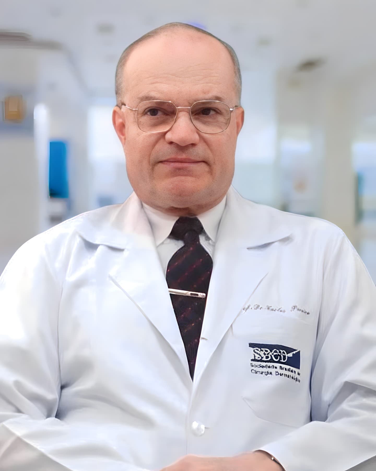 Dr. Carlos Augusto Zanardini Pereira, dermatologista em Curitiba, senhor simpático, poucos cabelos, aparentemente sentado em seu consultório, em olhando de lado, sorrindo discretamente, usando óculos, gravata e vestindo jaleco branco, por trás um corredor desfocado aparentemente de uma clínica.